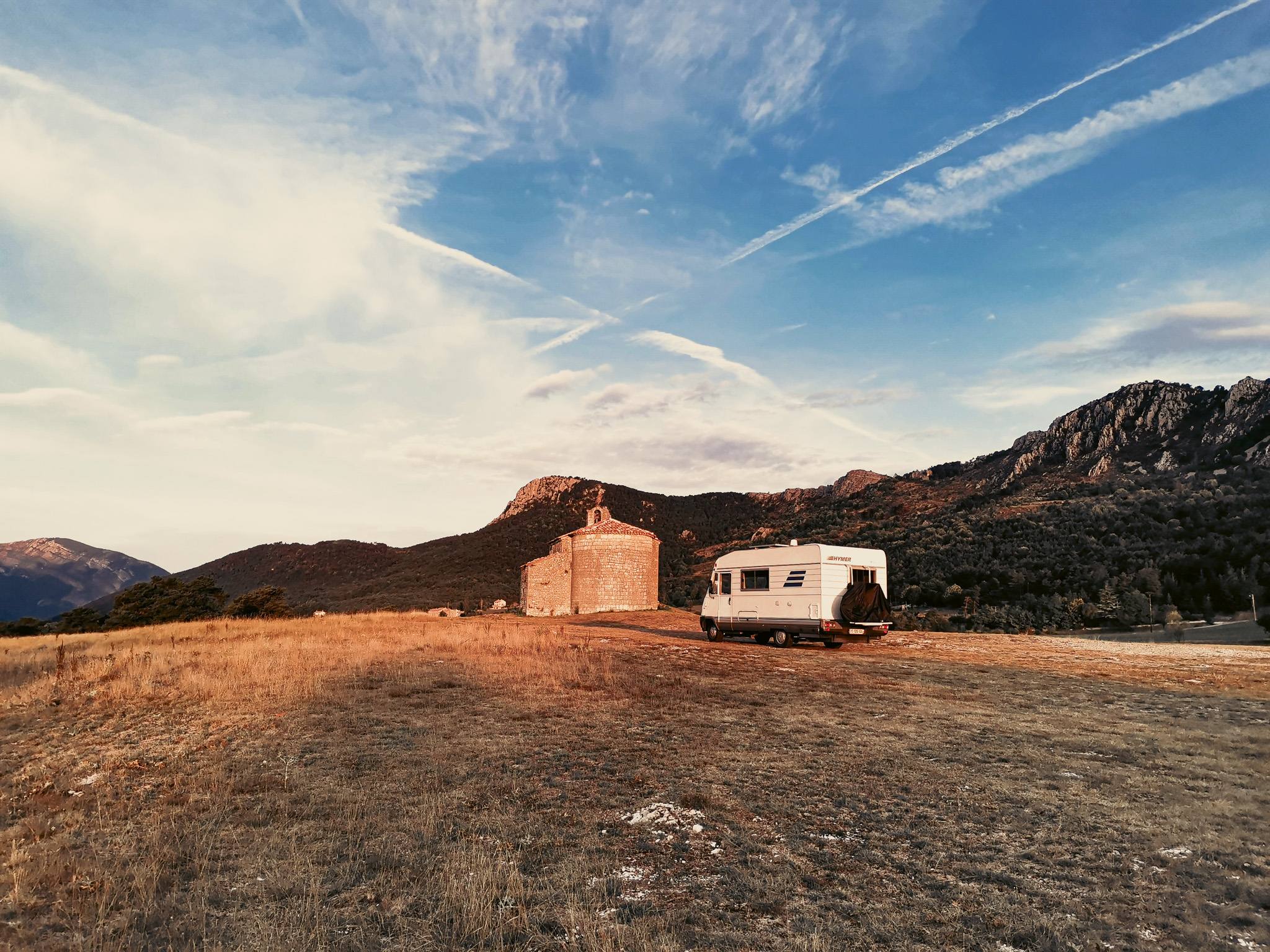 Motorhome Edouard is parked in front of a stone chapel surrounded by mountains, symbolizing the mobility and tax flexibility of the nomad.