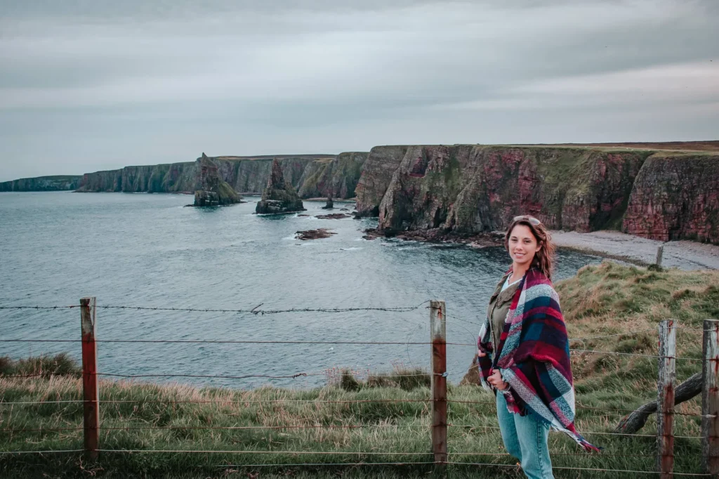 Caroline in front of the spectacular cliffs of John o'Groats with the sea and the rock formations