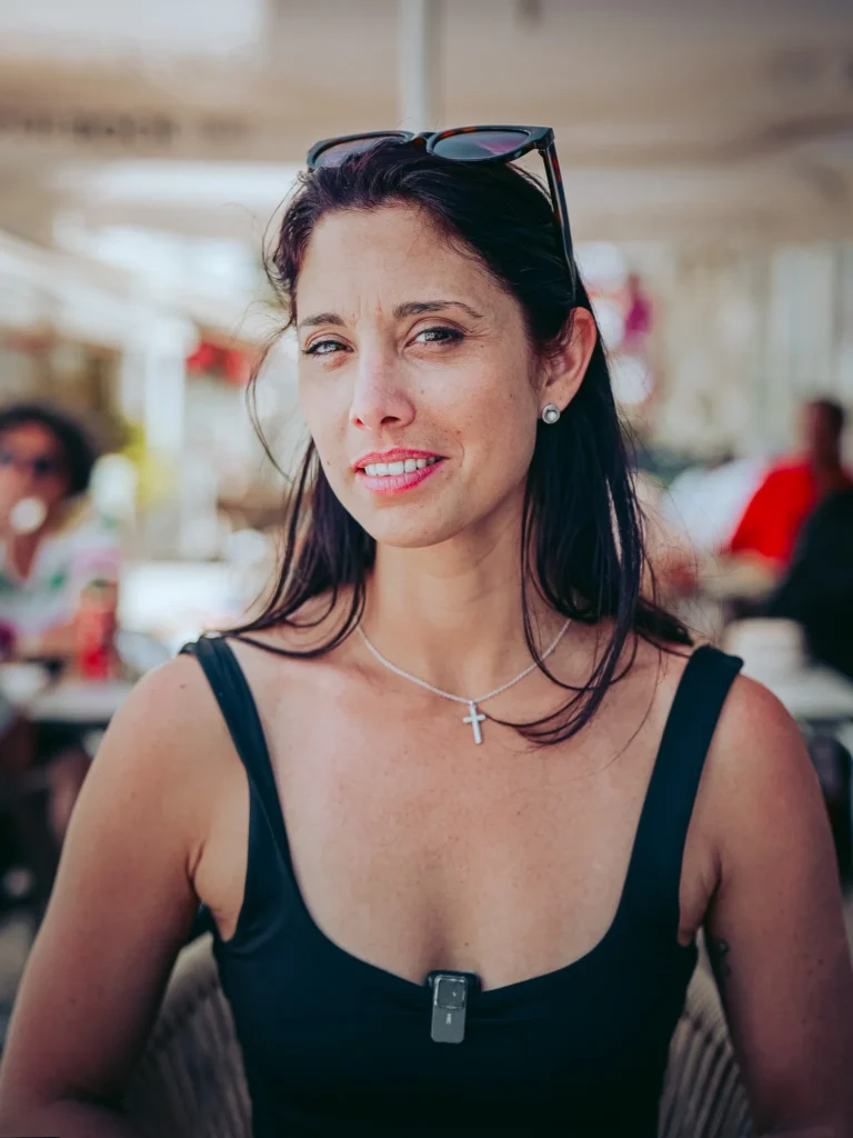 Caroline sitting on the terrace of a restaurant in Portimao, Algarve, on a sunny day, wearing a black tank top and a cross necklace.