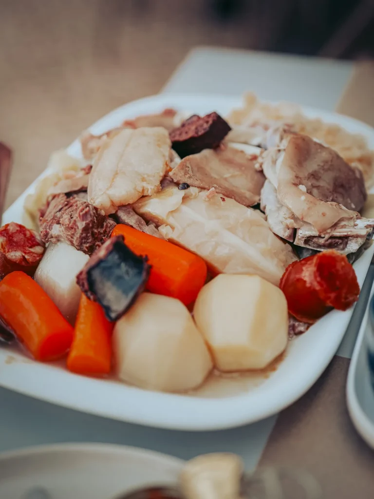 Portuguese cozido dish served on a plate, consisting of various meats, potatoes, carrots, cabbage, and pieces of sausage.