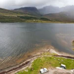 Aerial view of a loch on the Isle of Skye with a camper van parked by the water and misty mountains