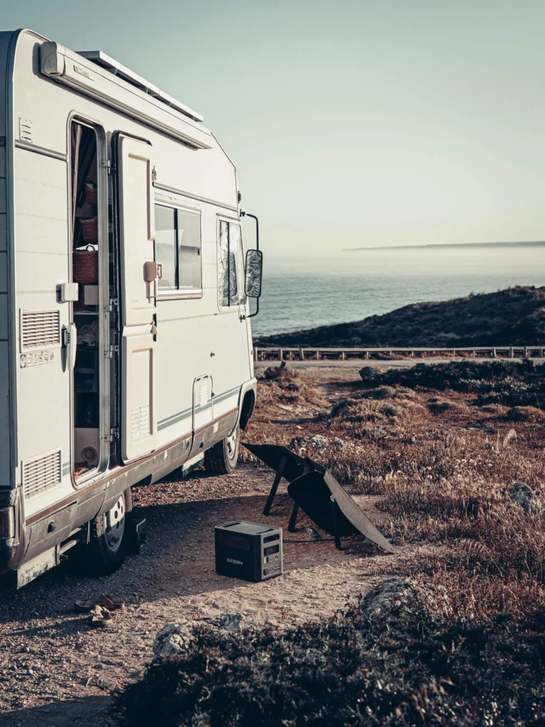 Motorhome parked by the sea with the Aferiy Nomad 1800 electric station and a solar panel on the ground