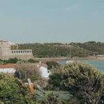 View of the Vila Nova de Milfontes fort and the Mira River, with white houses and a beach in the background under a clear sky.