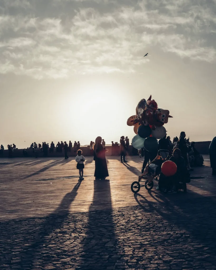 Street scene in Essaouira, Morocco at the end of the day, with silhouettes of passersby and a balloon seller in front of the setting sun.