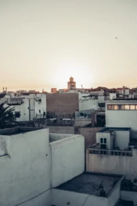White roofs of the medina of Essaouira at sunset, with the silhouette of a tower in the background.
