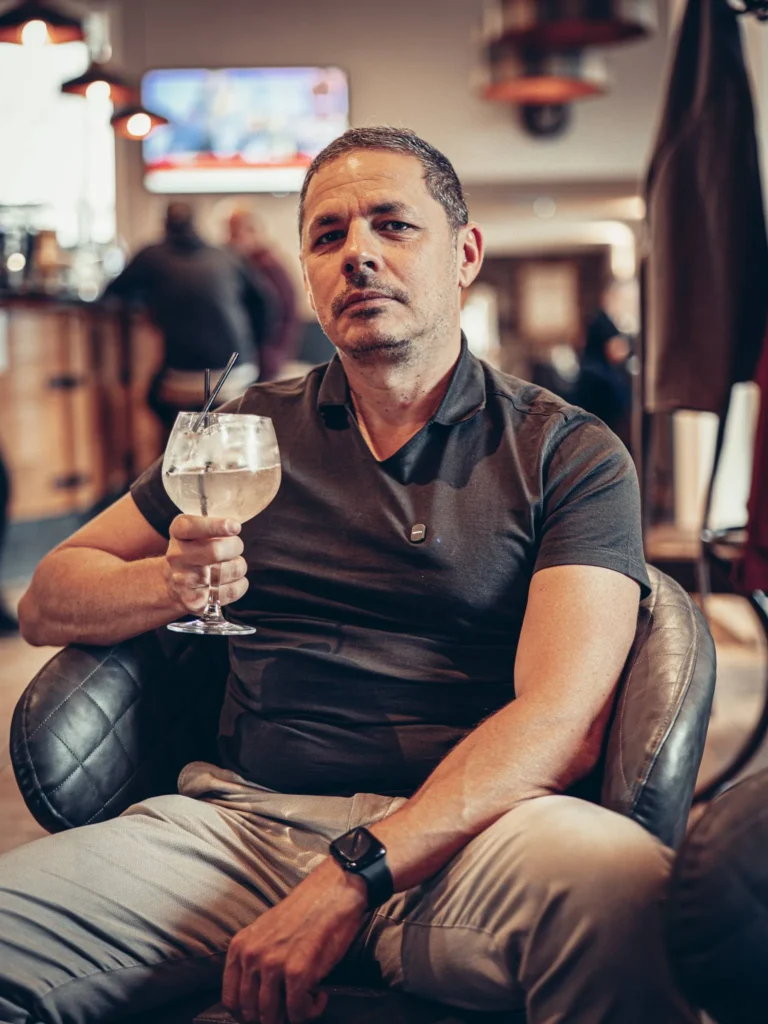 Xavier sitting in an armchair at the bar of the Allan Park Hotel in Stirling, Scotland, holding a cocktail glass, relaxed indoor atmosphere.