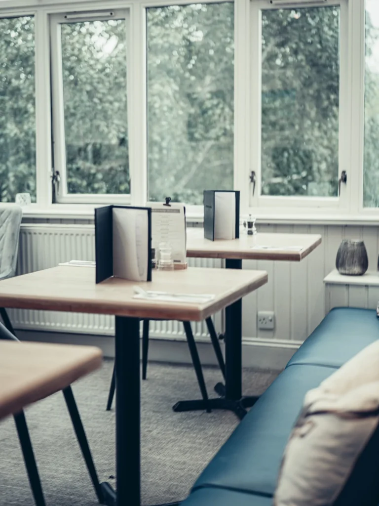 Bright dining room of the Allan Park Hotel in Stirling, featuring wooden tables, a blue bench, and large windows overlooking the greenery.