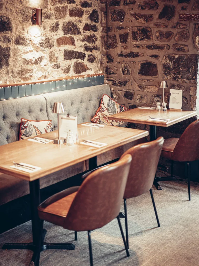Cozy restaurant corner at the Allan Park Hotel in Stirling, with exposed stone walls, grey banquette, and set tables.