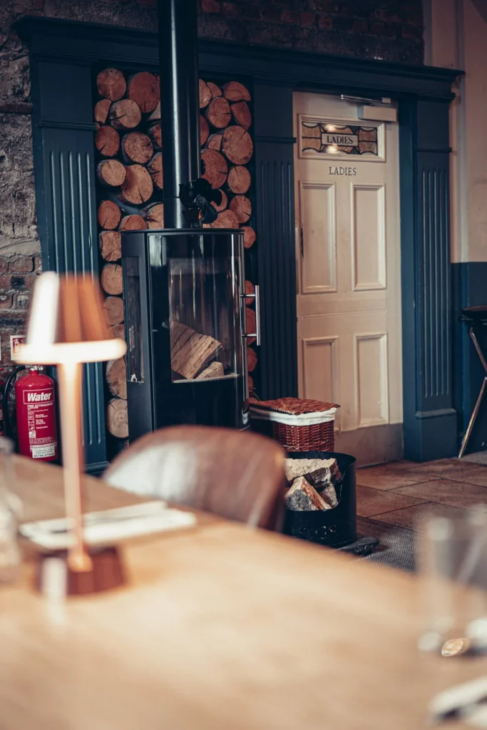 Warm corner of the Allan Park Hotel restaurant in Stirling, featuring a wood stove, stacked logs, and a door indicating the ladies' restroom. Typical cozy atmosphere of a Scottish establishment.
