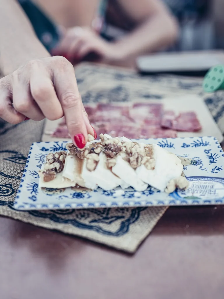 Fresh goat cheese plate with honey and walnuts (Monte Pereiro) at Bodeguita Salinas in Tavira: Caroline's hand is serving, with a plate of Iberian ham in the background.