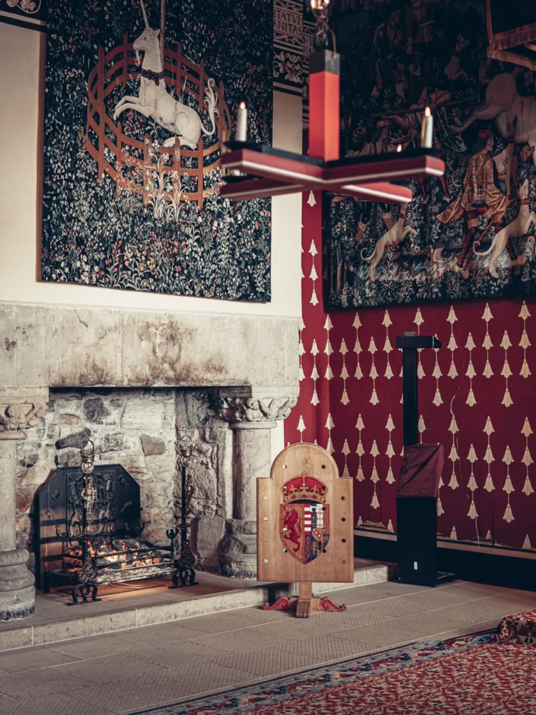 A stone fireplace in a richly decorated room at Stirling Castle, with the unicorn tapestries and a royal shield hanging beside the hearth.