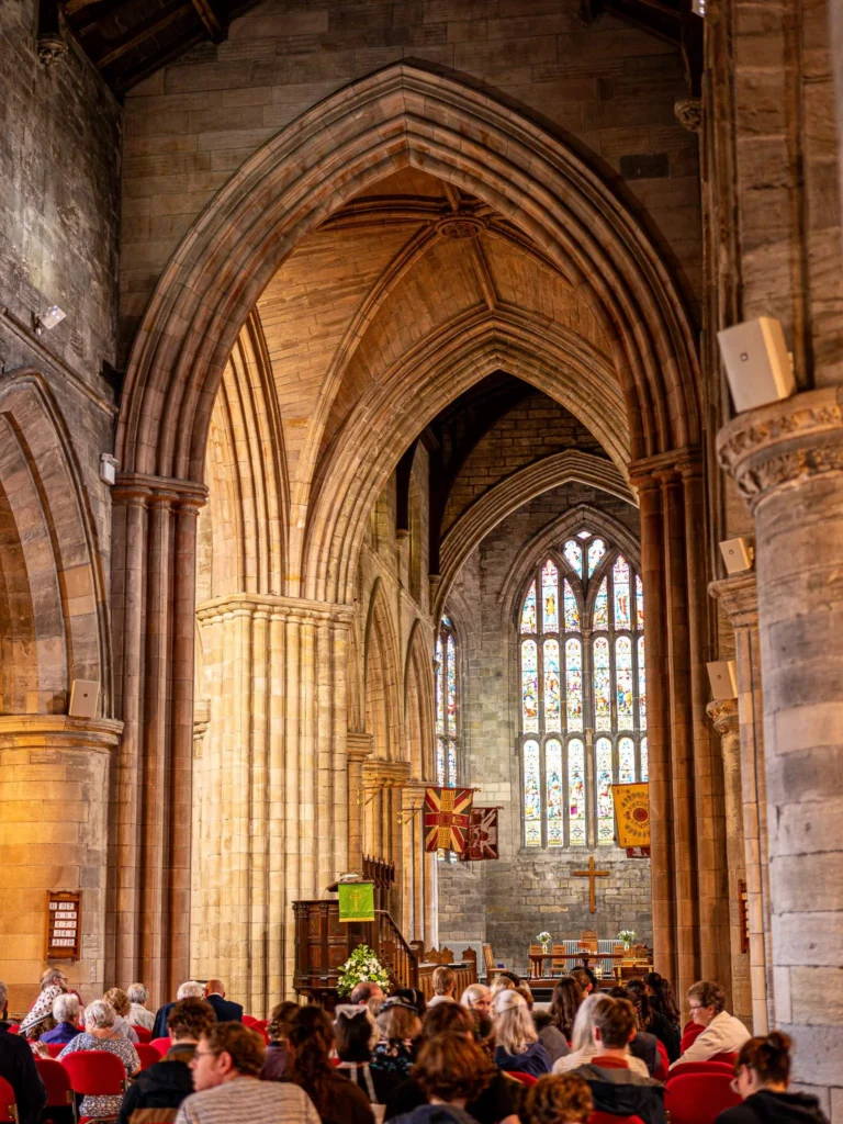 Interior of the Church of the Holy Rude in Stirling: large stone arches, wooden beamed ceiling, and exposed beams, stained glass at the back. The interior is much more impressive than the facade would suggest.