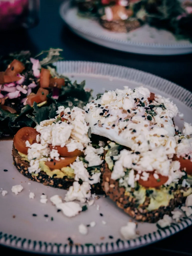 Plate of seed bread toast topped with avocado, cherry tomatoes, and fresh cheese, accompanied by a colorful salad, served in a restaurant in Lagos in the Algarve.