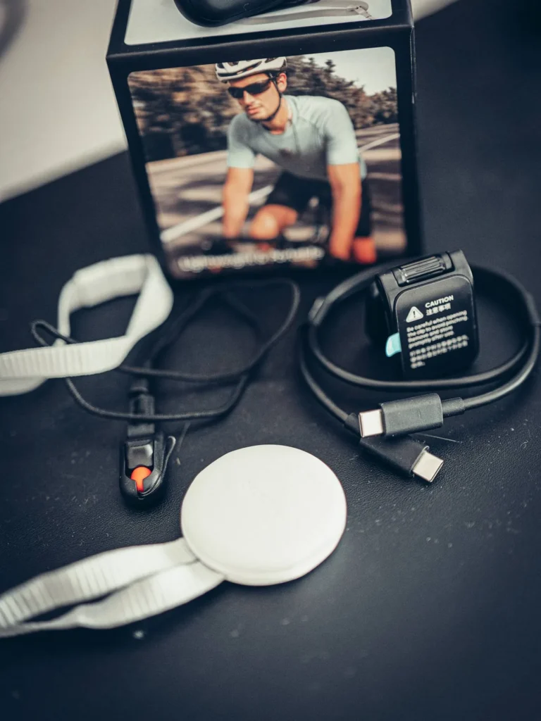 Nahaufnahme des Zubehörs der Insta360 GO Ultra: Clip mit orangefarbenem Entriegelungsknopf, runde Magnethalterung und doppeltes USB-C-Kabel.