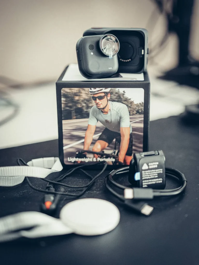 Der komplette Lieferumfang der Insta360 GO Ultra: die Kamera auf dem Action Pod, die Halskette, der Magnetclip, die Halterung und das USB-C-Kabel ausgebreitet.