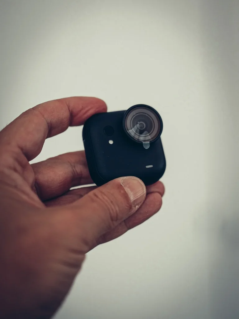 Das Kameramodul der Insta360 GO Ultra in der Hand gehalten, Vorderseite mit Objektiv und Mikrofon, vor hellem Hintergrund.