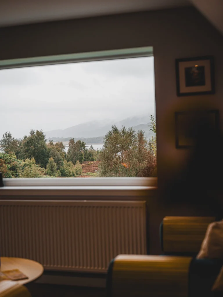View from inside a house overlooking a misty woodland landscape of the Scottish Highlands through a large window.