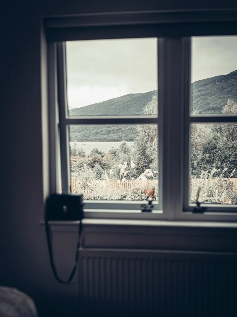 View of the lush green mountains of the Scottish Highlands through the window of a room at Rocklee Bnb in Glencoe, on a cloudy day.