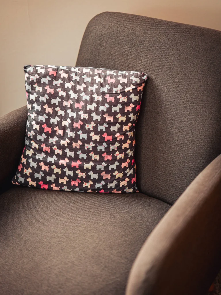 Scottish dog patterned cushion placed on a brown fabric armchair in a cosy interior in Glencoe, Highlands.