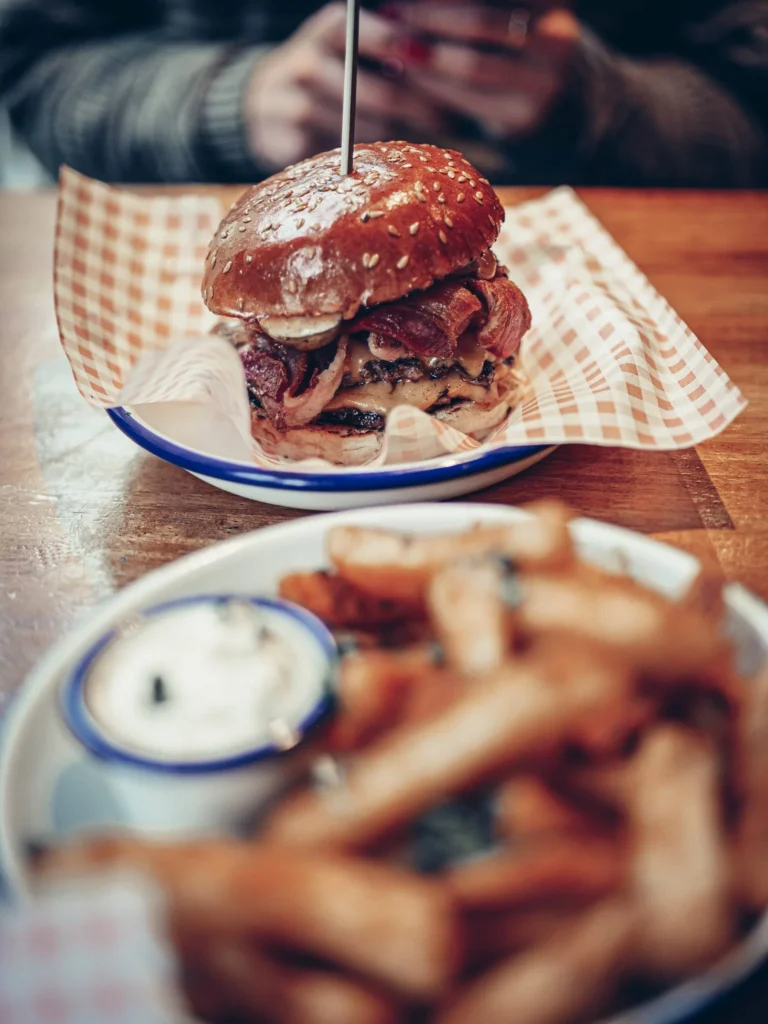 A bacon and cheese burger served on checked paper with fries and a sauce pot at Slanj-A-Va, Stirling.