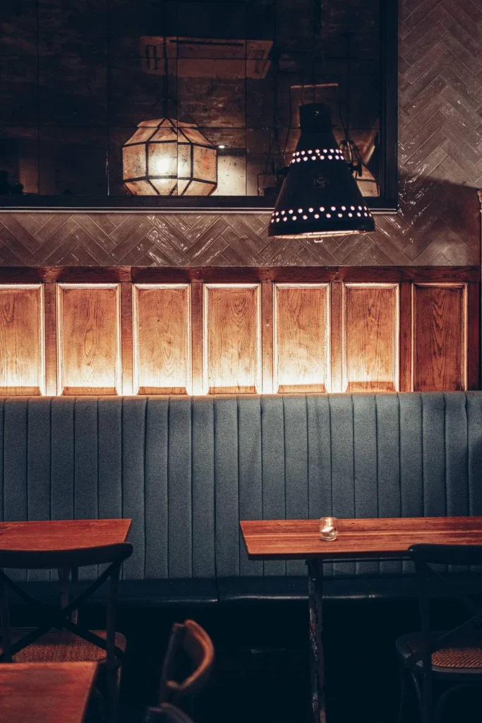 Blue velvet banquette and wooden tables in one of the rooms at Stravaigin, Glasgow, with panelling and large metal pendant lights.