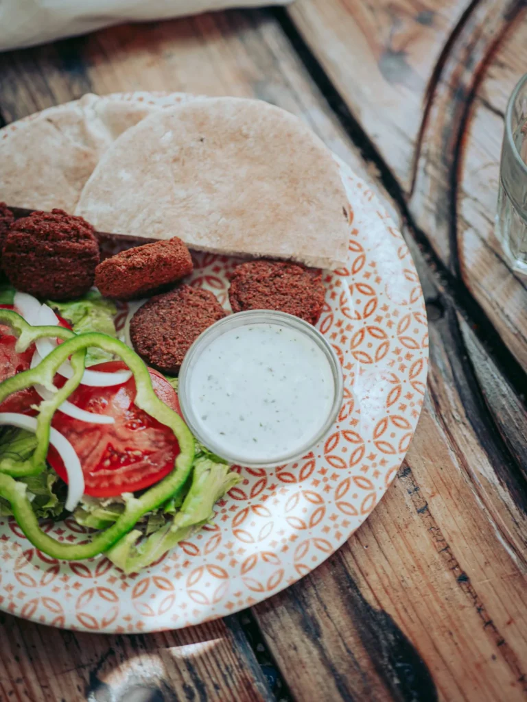 Falafel plate with pita bread, raw vegetables, and white sauce on a wooden table at The Garden Bar and Grill in Lagos.