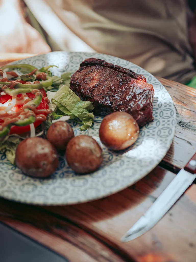 Grilled meat served with potatoes and a salad on a wooden table at The Garden Bar and Grill in Lagos.