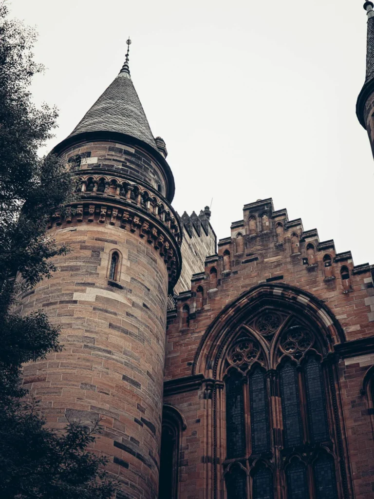 Tower and stone facade of the University of Glasgow, stained glass and sculpted details.