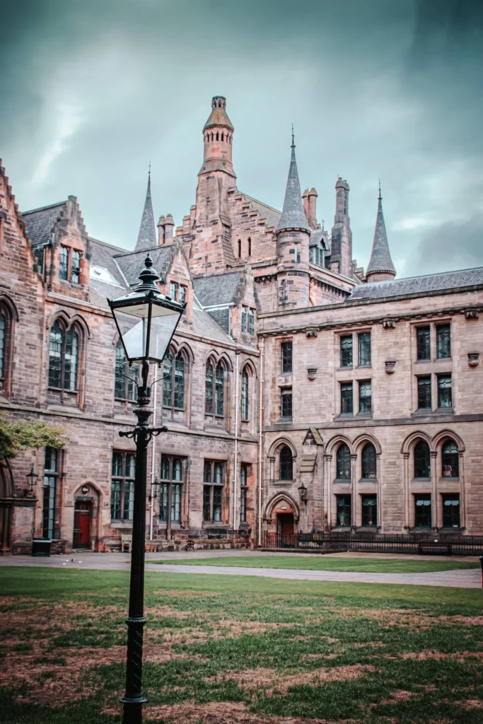 Inner courtyard of the University of Glasgow, featuring Gothic architecture and an old lamppost under a cloudy sky.