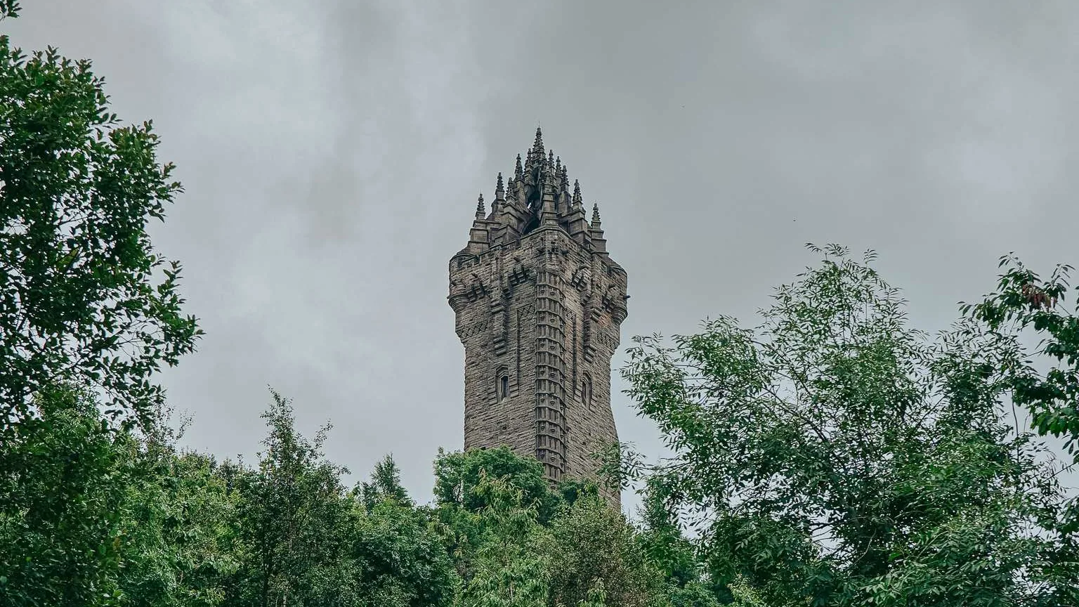 The Wallace Monument rises above the Abbey Craig forest under a cloudy sky, Stirling, Scotland