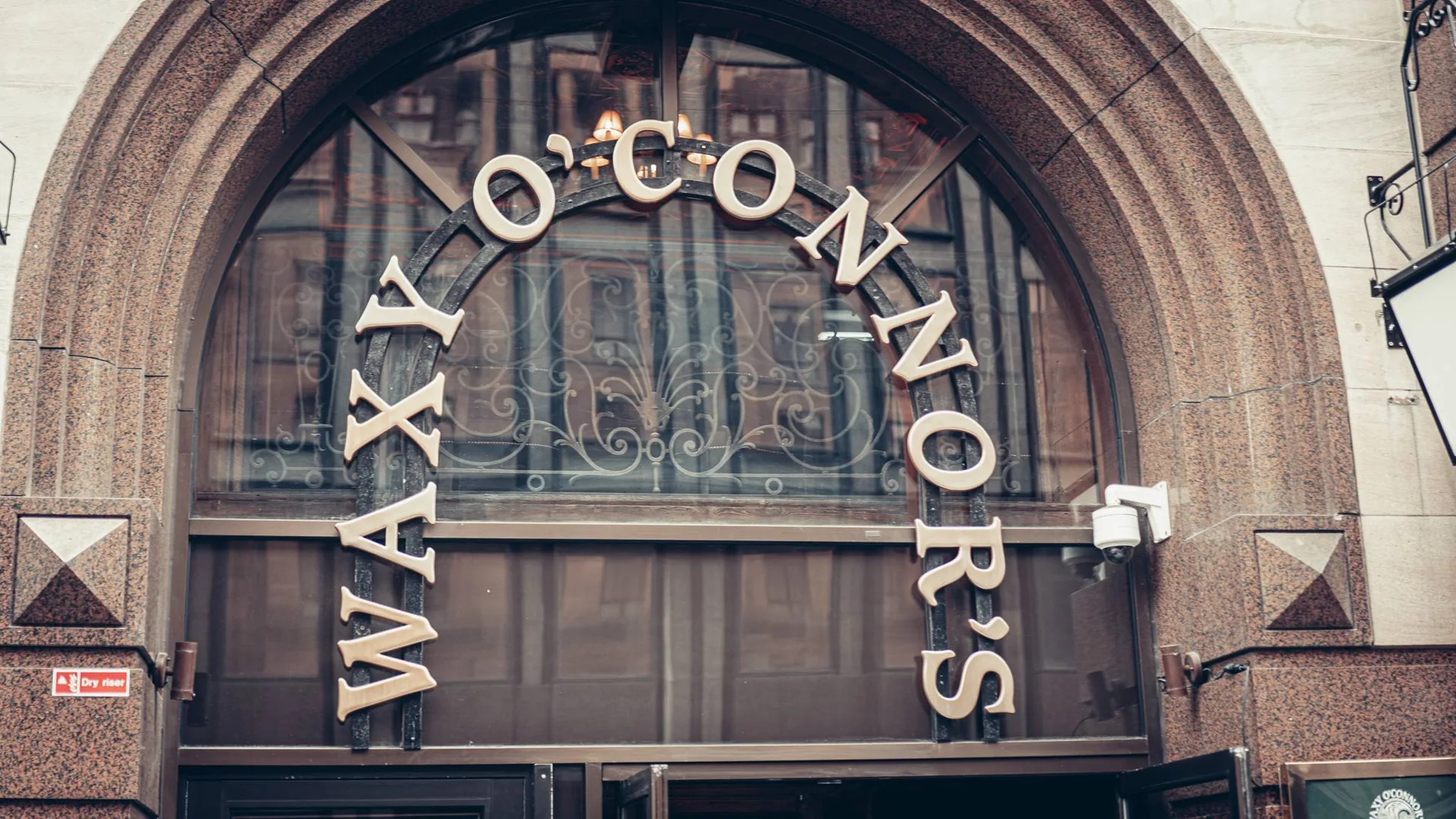 The stone facade of Waxy O'Connor's at 44 West George Street in Glasgow, with its large arch and pub sign.