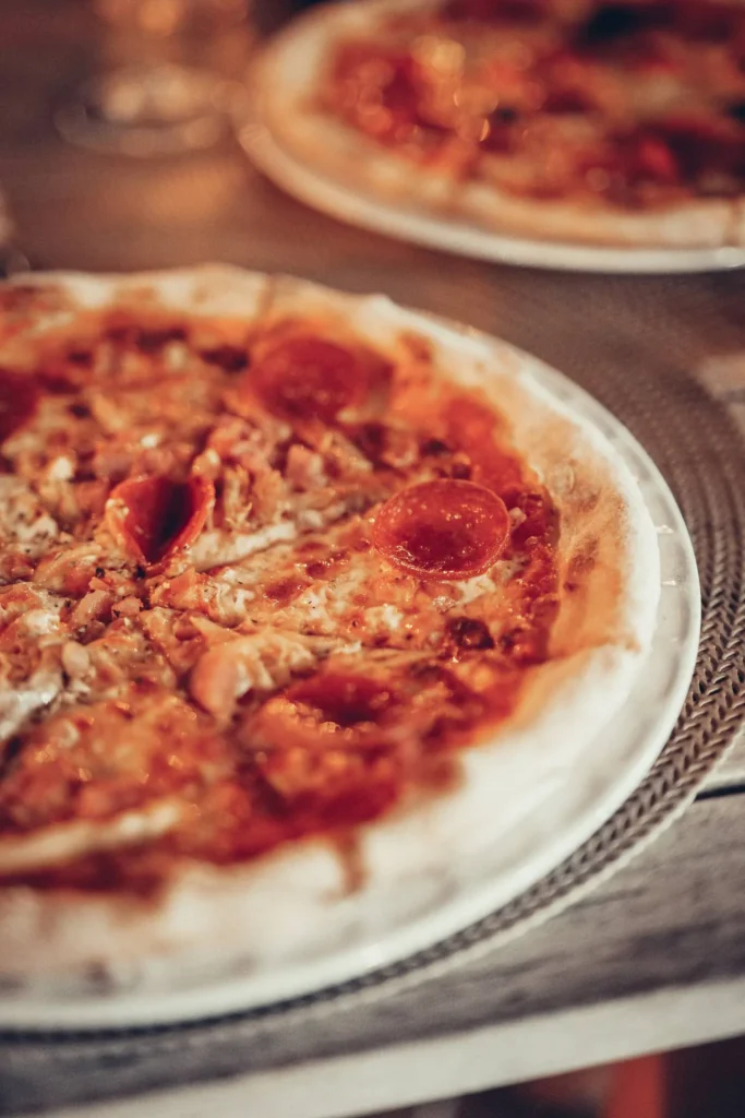 Two pizzas topped with pepperoni and cheese are placed on a restaurant table, warm indoor atmosphere.