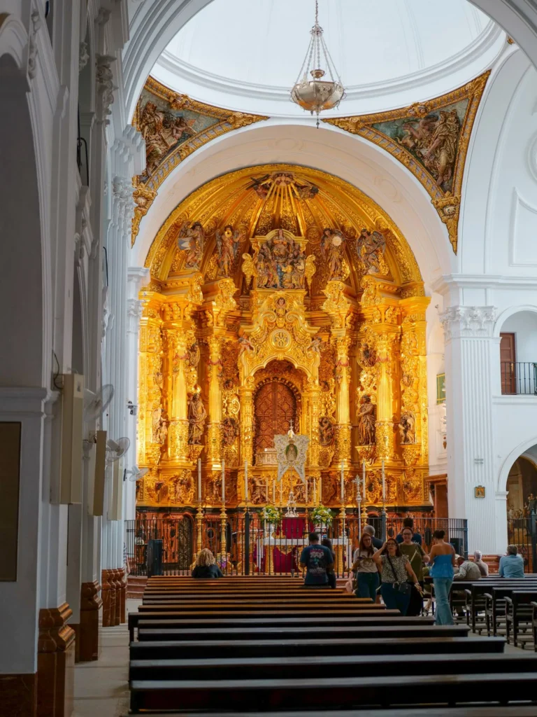 Vergoldeter Altaraufsatz und weißer Innenraum der Wallfahrtskirche von El Rocío mit Besuchern bei den Bänken